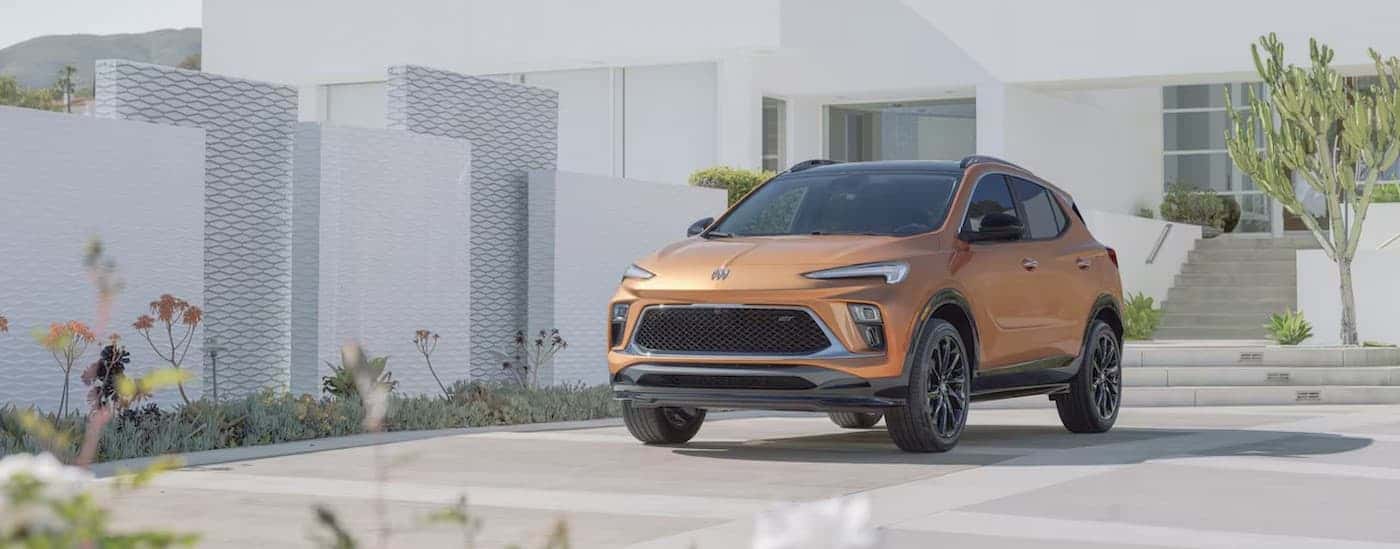 An orange 2024 Buick Encore GX parked near a house.