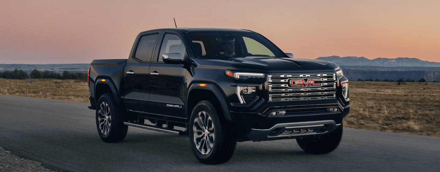 Black 2026 GMC Canyon driving down a road at dusk