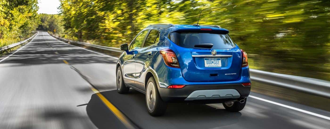 Blue 2019 Buick Encore from the rear driving down a tree-lined road.