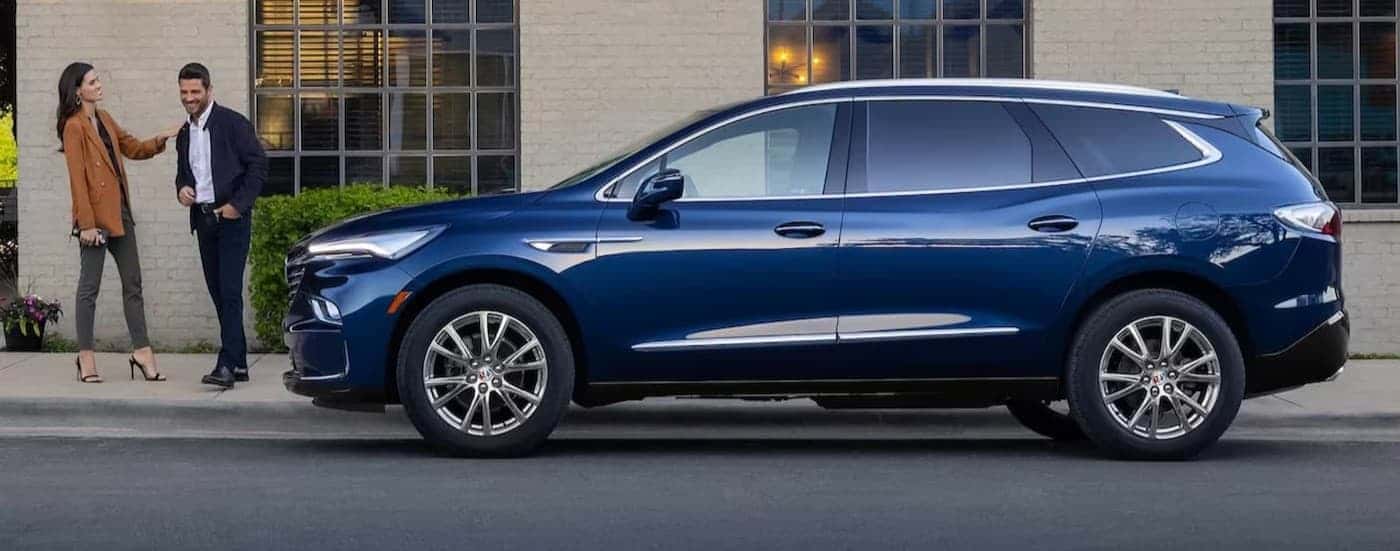 Two people walking near a blue 2024 Buick Enclave.