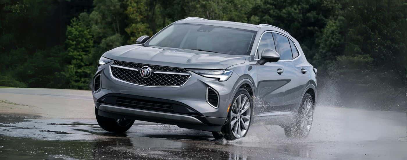 A silver 2023 Buick Envision Avenir shown driving on wet ground.