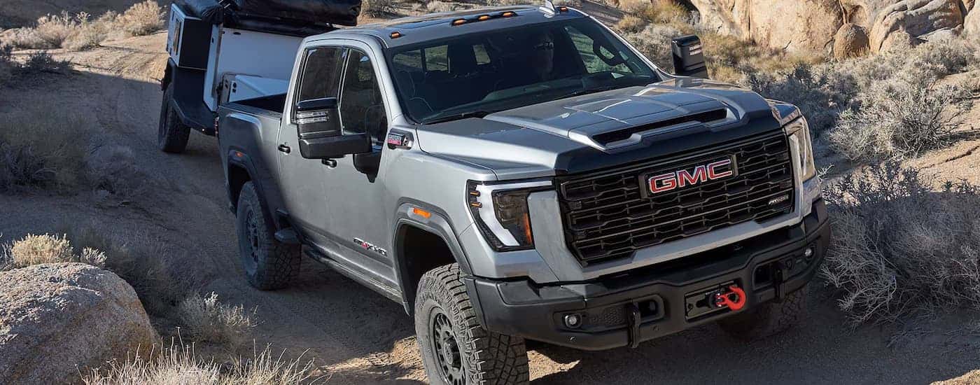 A silver 2026 GMC Sierra 2500 HD off-roading while towing a trailer