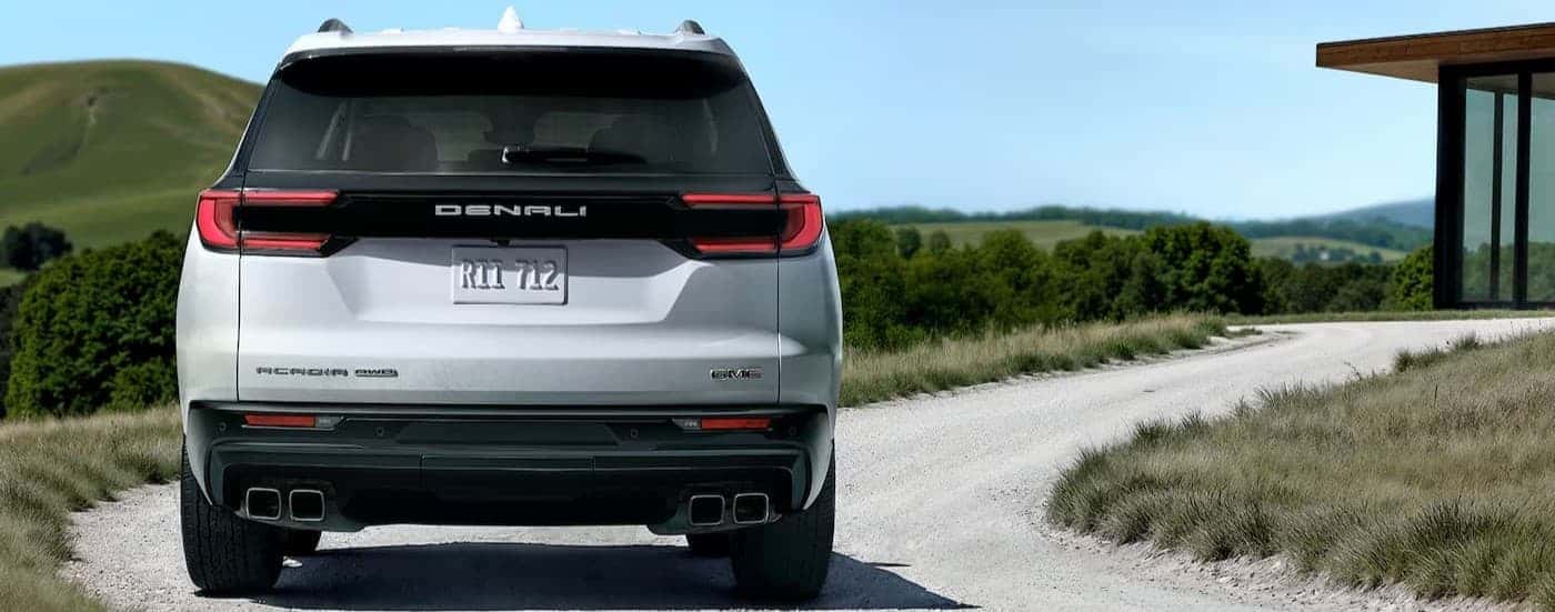 A white 2026 GMC Acadia Denali driving on a road.