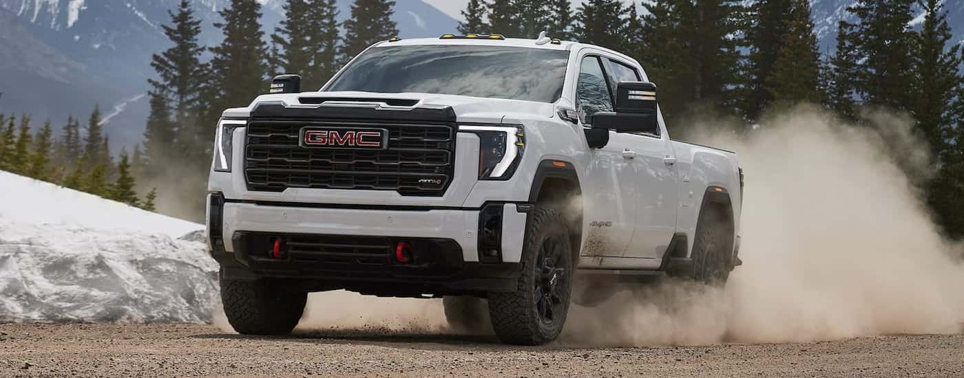 White 2026 GMC Sierra 2500 HD driving off-road on a dirt road.