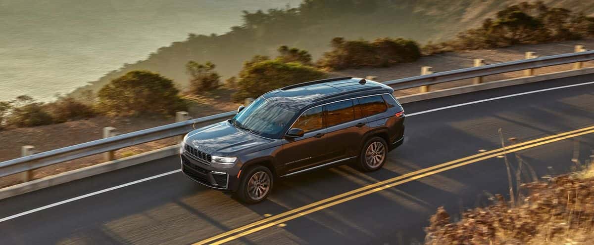 Dark gray 2026 Jeep Grand Cherokee L seen from above driving along a curving coastal road