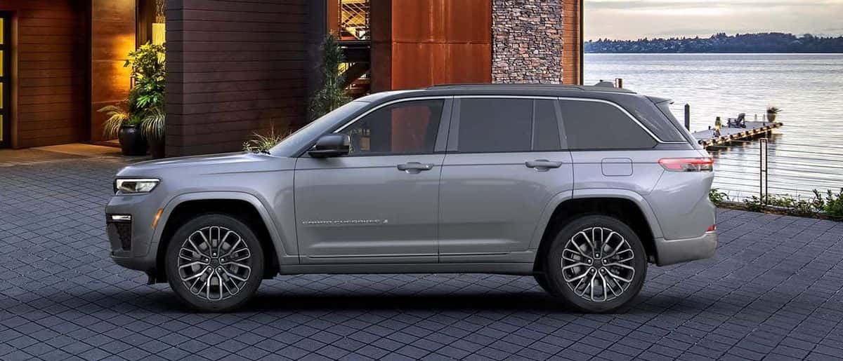 Silver 2026 Jeep Grand Cherokee Summit two-row SUV in side profile parked beside a lake