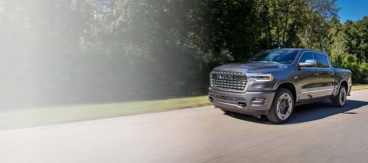 Gray 2026 Ram 1500 Limited 4x4 Crew Cab driving down a tree-lined country road