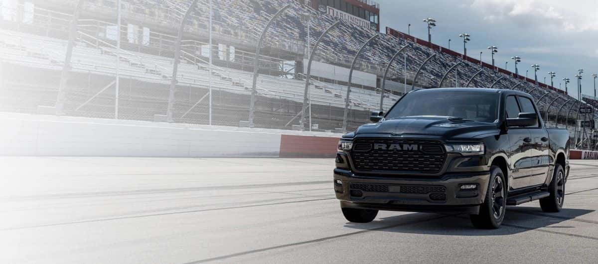 Black 2026 Ram 1500 Warlock 4x4 Crew Cab parked on a race track in front of grandstands