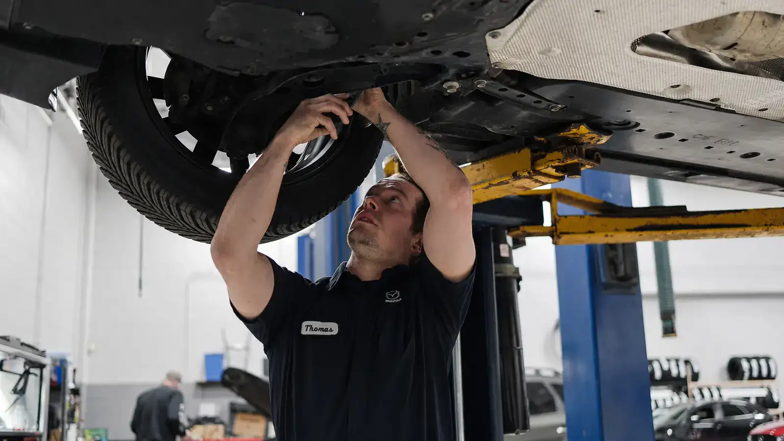 Mazda technician performing undercar service on a vehicle raised on a lift