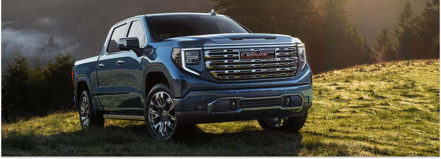 Blue 2026 GMC Sierra 1500 parked in a grassy field, viewed from a front three-quarter angle.