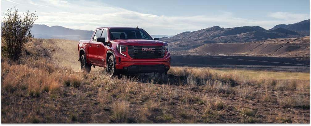 Front three-quarter view of a red 2026 GMC Sierra 1500 pickup truck driving through a mountainous landscape.