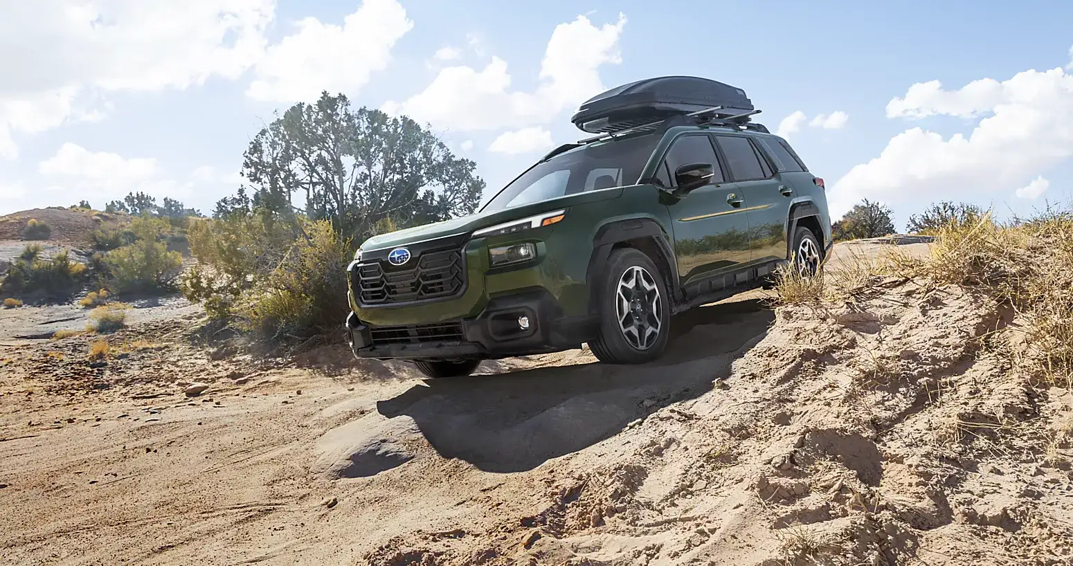 2026 Subaru Outback in green with a rooftop cargo box parked on an off-road trail.