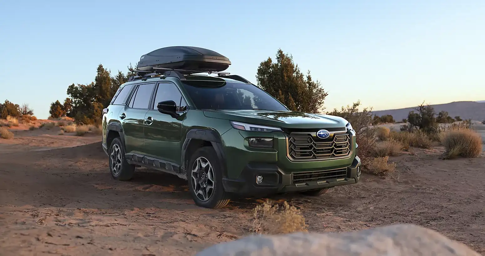 2026 Subaru Outback in green driving on a rugged off-road trail with a rooftop cargo box.