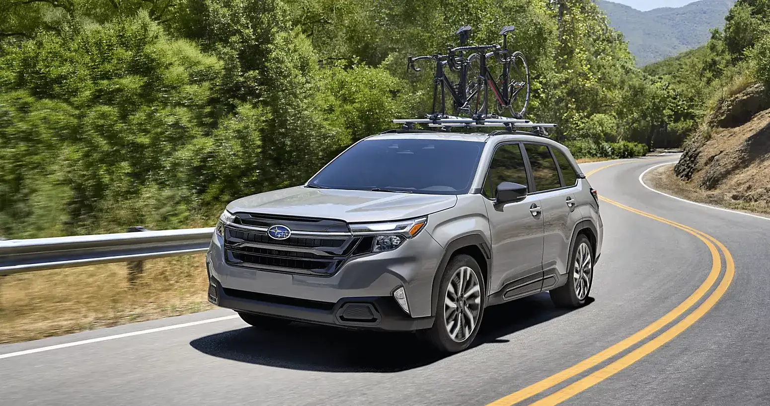 2026 Subaru Forester driving on a winding mountain road with bicycles mounted on the roof rack.