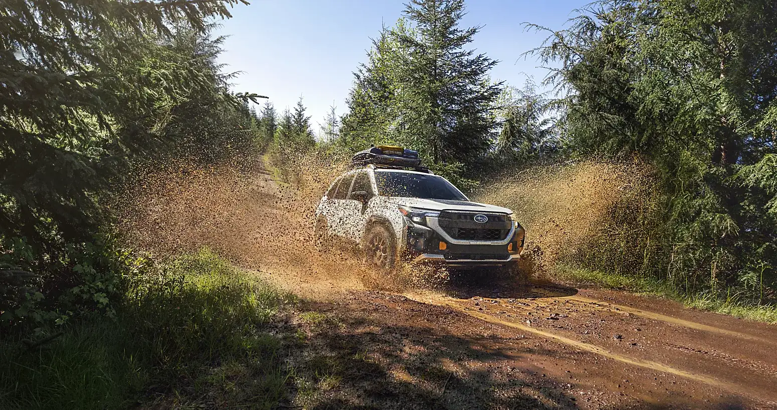 2026 Subaru Forester driving through a muddy forest trail with mud spraying around the vehicle.