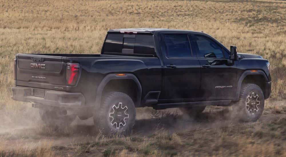 A black 2026 Sierra 2500 HD shown driving in a field from the side.