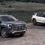 A blue 2026 GMC Terrain Denali and a white 2026 GMC Terrain AT4 parked by a field.