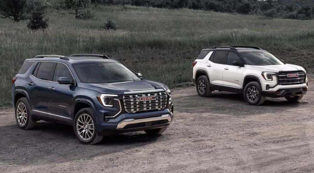 A blue 2026 GMC Terrain Denali and a white 2026 GMC Terrain AT4 parked by a field.