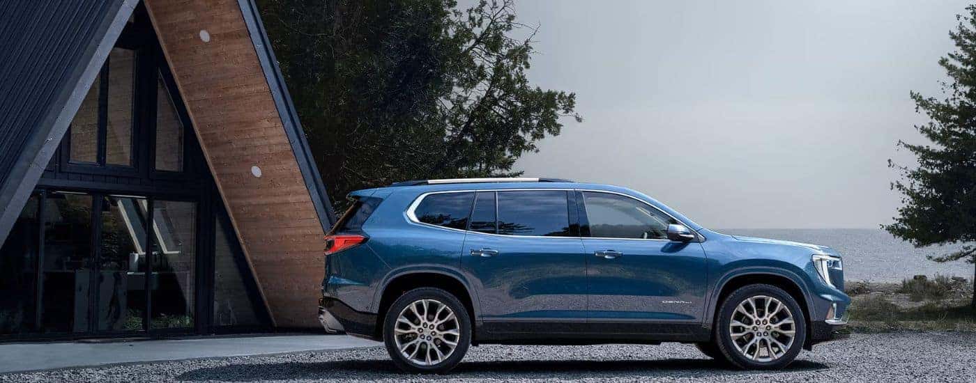 Blue 2026 GMC Acadia Denali parked in front of a lakeside cabin