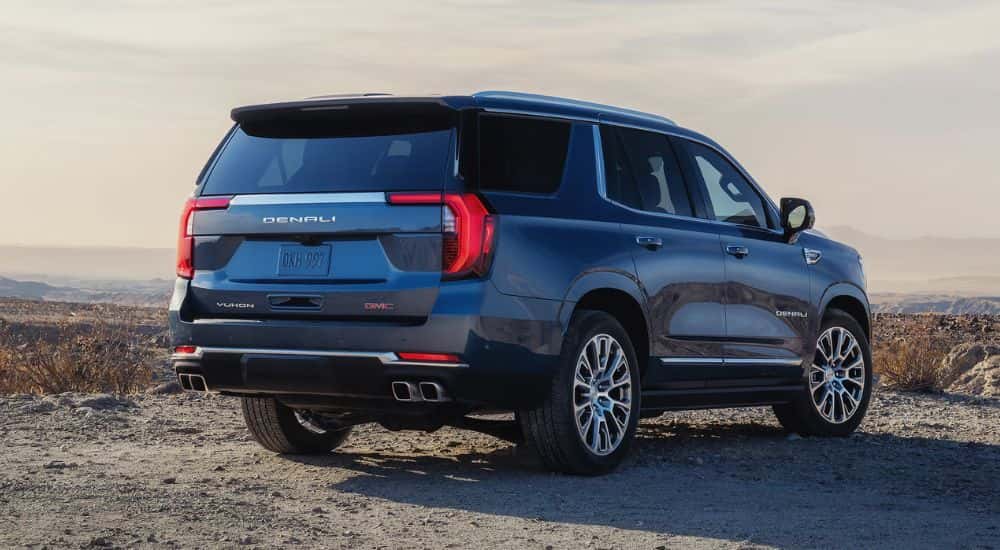 A blue 2026 GMC Yukon Denali shown from rear parked on rocky terrain.