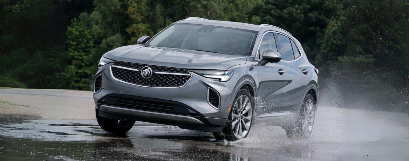 A silver 2023 Buick Envision Avenir shown driving on wet ground.