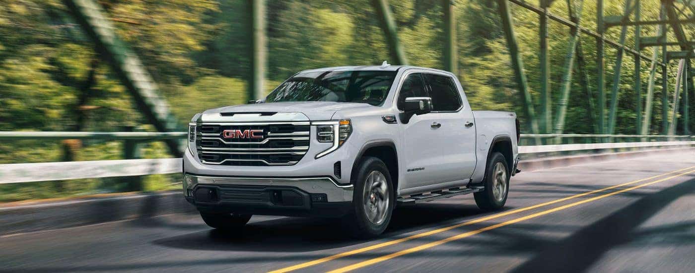 White 2026 GMC Sierra 1500 driving across a sunlight bridge.