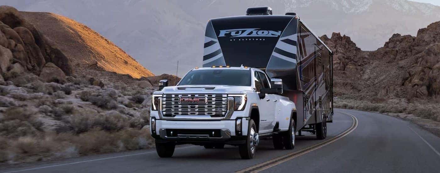 A white 2024 GMC Sierra 3500 HD Denali towing a trailer.