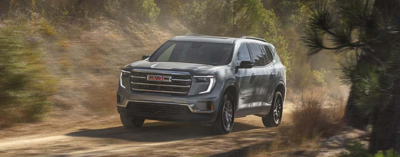 Grey 2025 GMC Acadia driving on a dirt road.