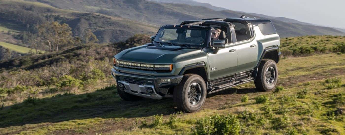 A green 2024 GMC Hummer EV driving on a trail.