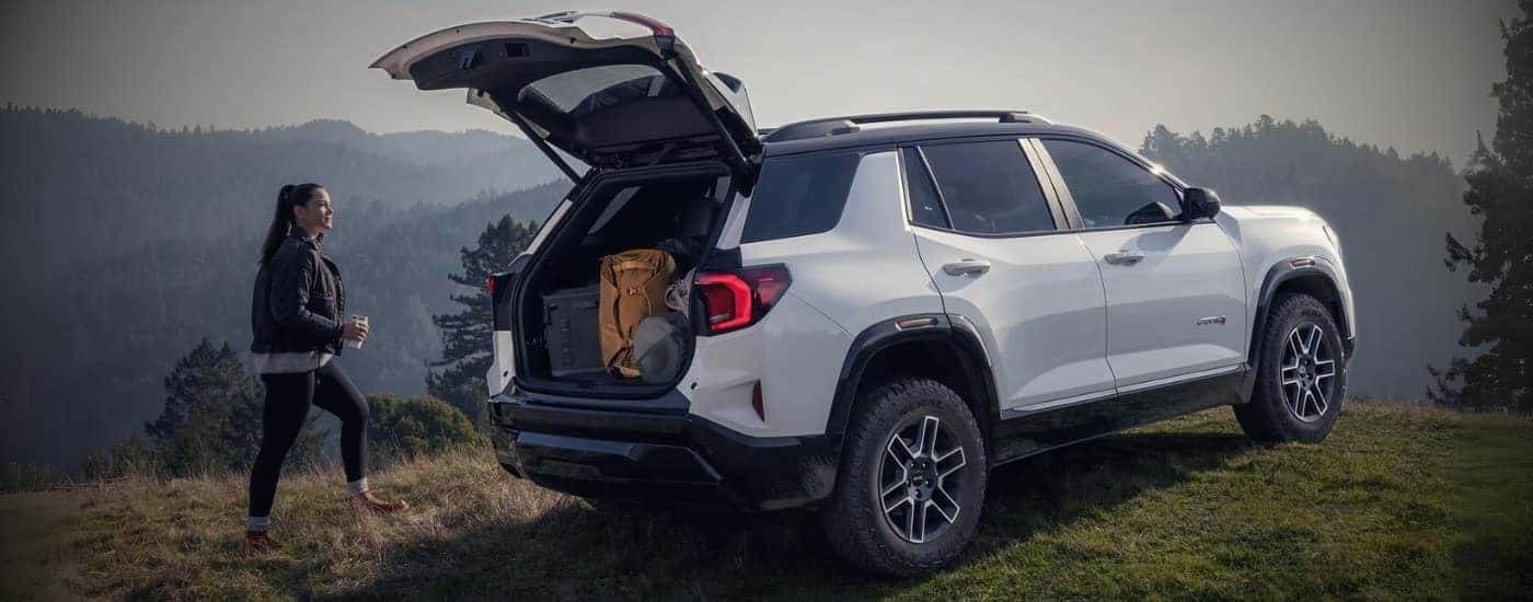A person approaching a white 2026 GMC Terrain AT4 with rear gate open.