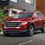 Red 2021 GMC Acadia SLE driving on a paved road.