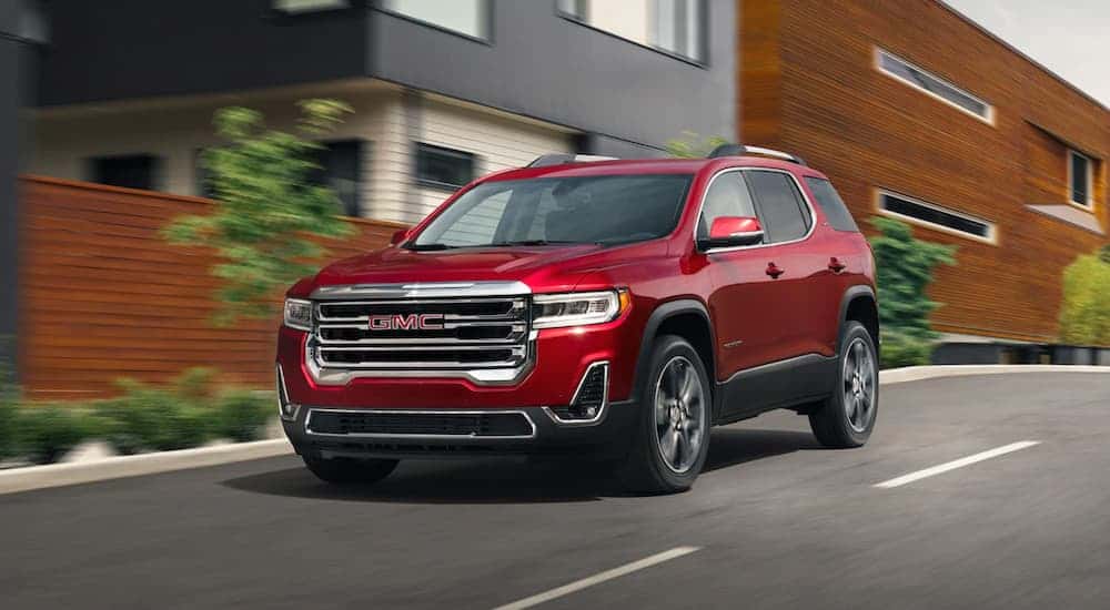 Red 2021 GMC Acadia SLE driving on a paved road.
