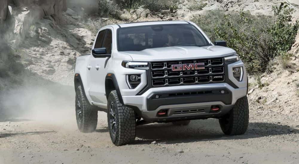 White 2023 GMC Canyon AT4 driving off-road on a dirt trail.