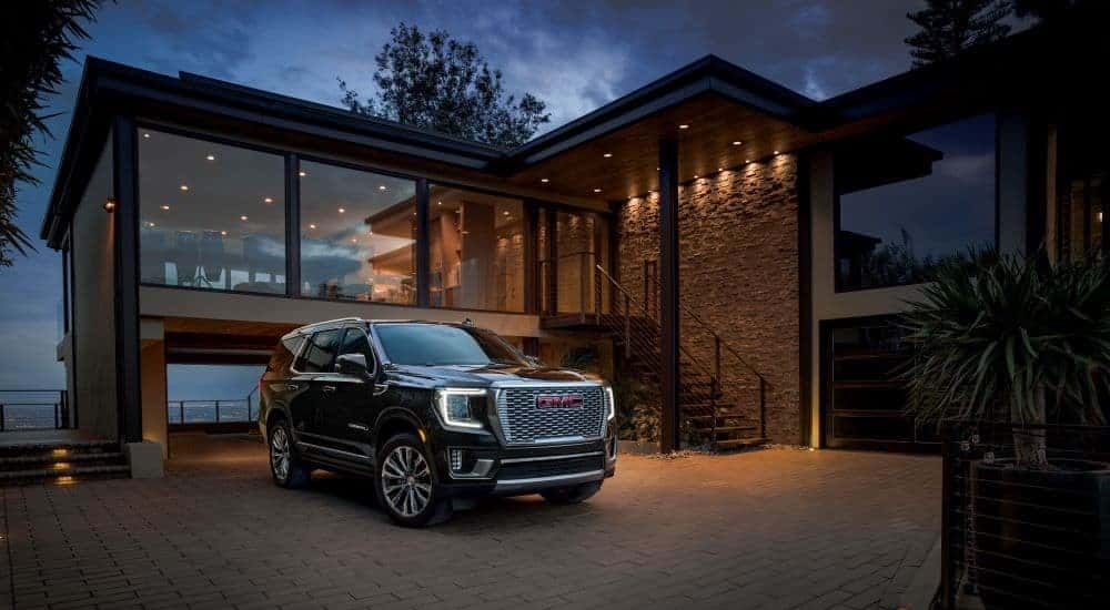 Black 2023 GMC Yukon Denali parked in a driveway of a modern house.
