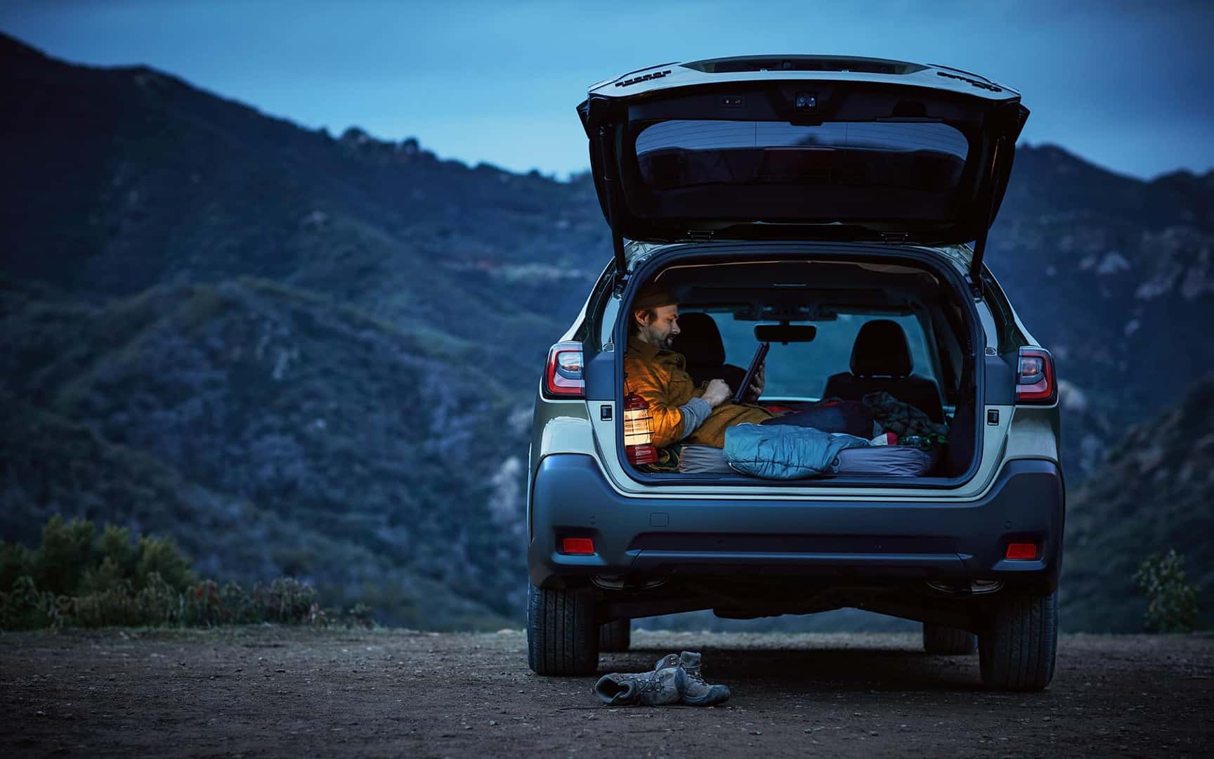 Rear shot of Outback Onyx Edition XT in Autumn Green Metallic parked at overlook and male talent sitting in open trunk holding a tablet