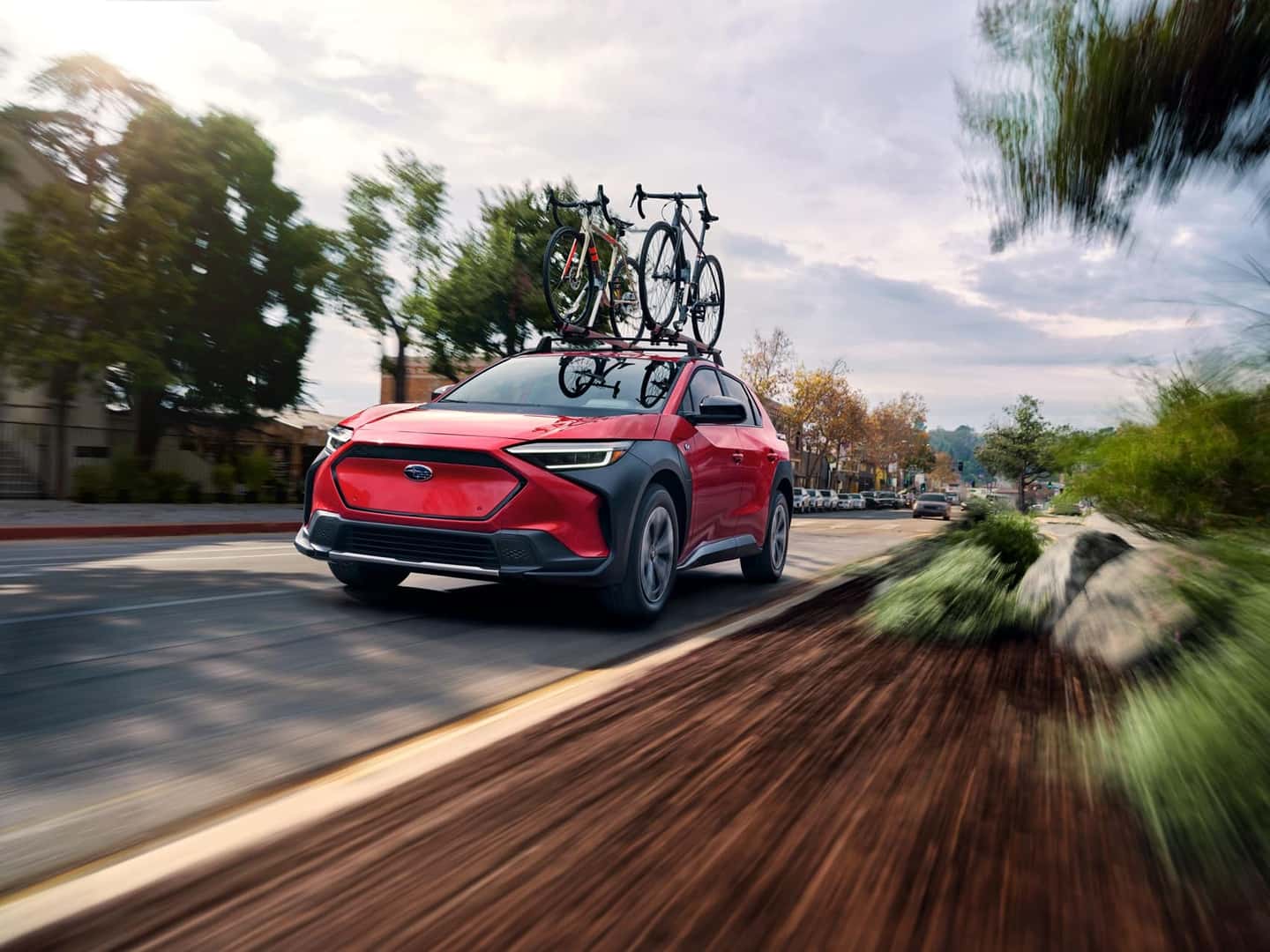 Red Subaru Solterra with a roof-mounted bike rack speeding through a sun-drenched suburban street