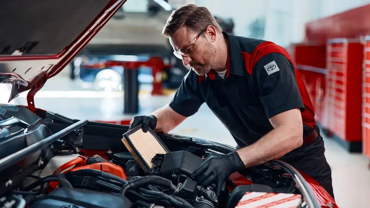 Toyota technician in safety glasses inspecting an engine filter under an open hood