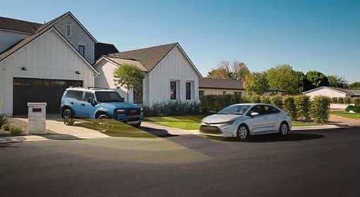 A blue Toyota SUV in a driveway and a white Toyota sedan on a neighborhood street