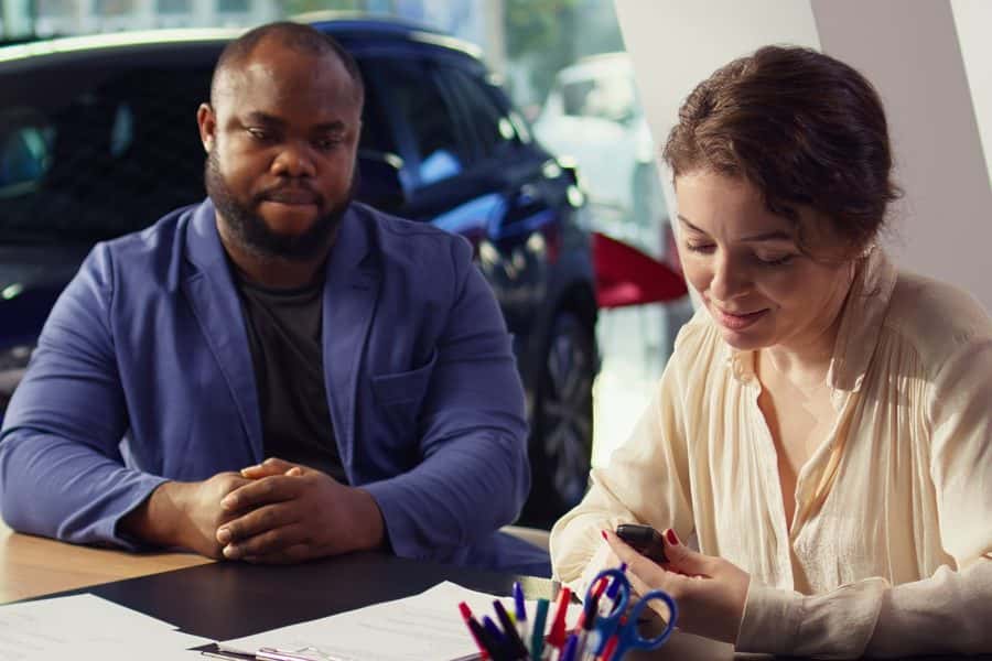 Two customers review paperwork at a desk in a dealership showroom