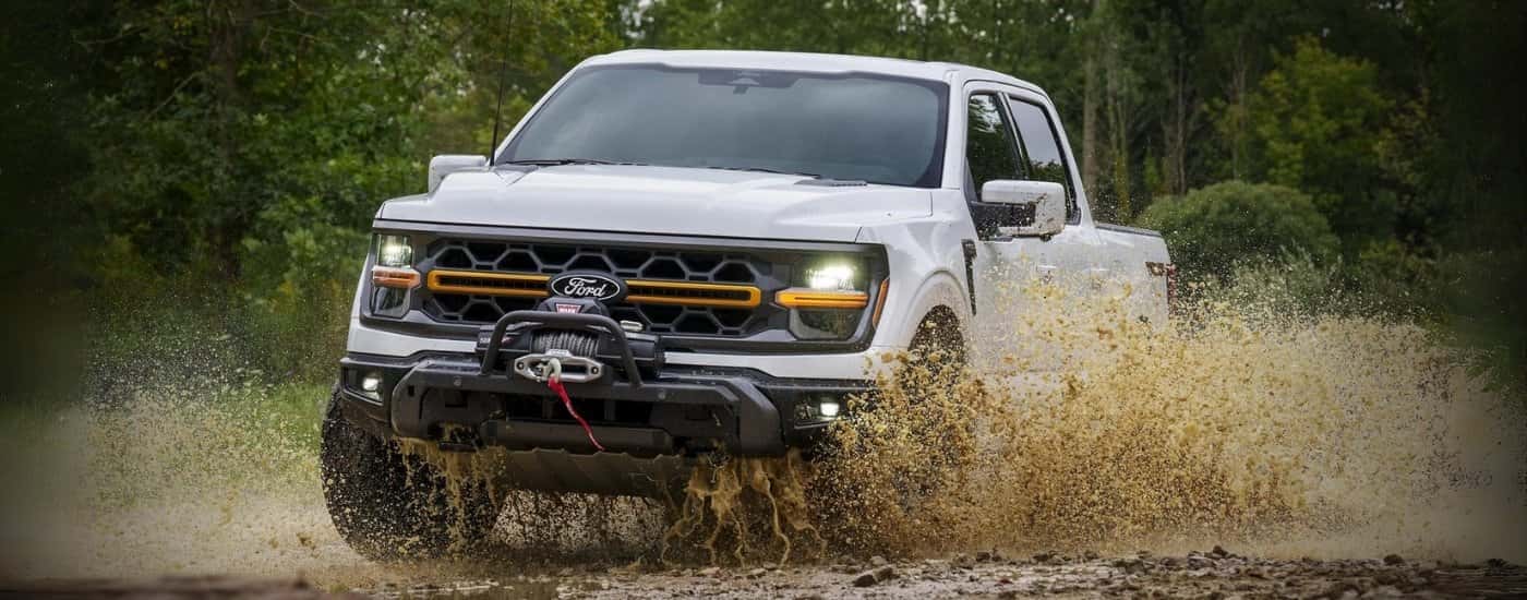A white 2026 Ford F-150 off-roading in mud