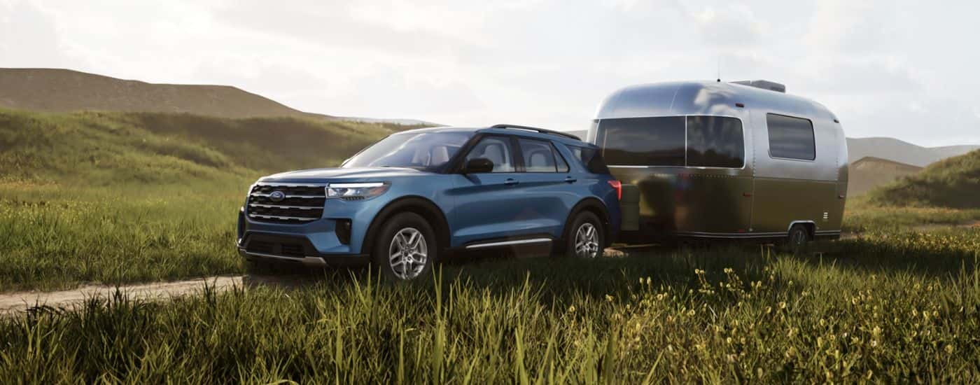 Blue 2026 Ford Explorer Active towing a camper in a field.
