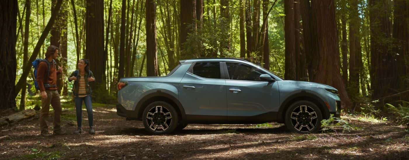 A blue 2026 Hyundai Santa Cruz Limited shown parked in the woods next to a couple.
