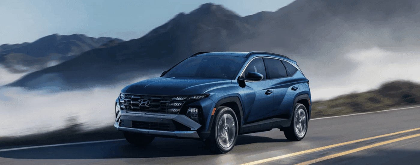 Blue 2026 Hyundai Tucson driving past misty mountains.