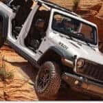 Front three-quarter view of a white 2026 Jeep Wrangler Willys climbing red rock terrain.
